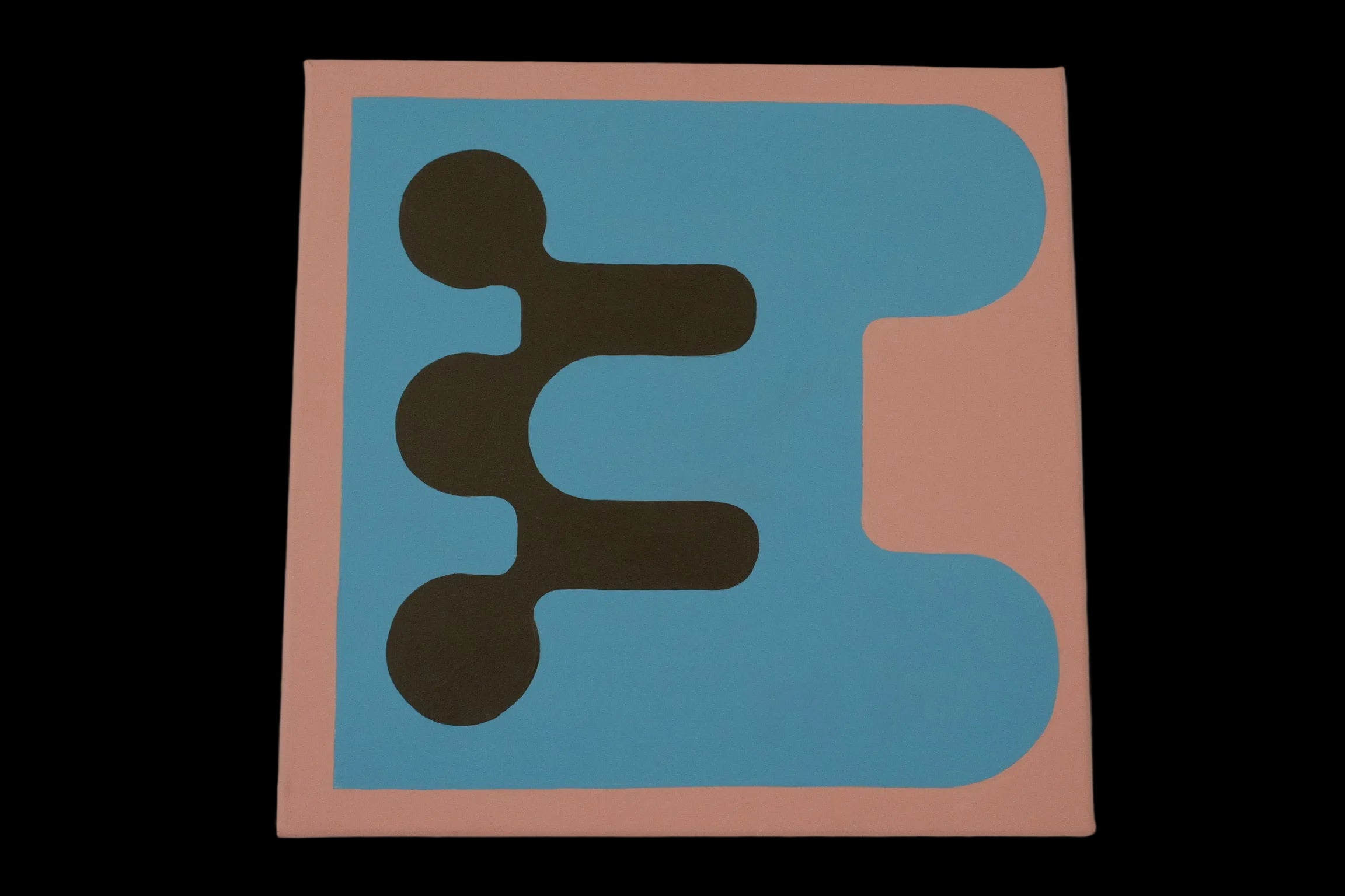 A square abstract art print or canvas featuring a minimalist geometric design with a peach border, a large light blue shape, and three dark brown circular and rectangular elements, displayed against a neutral gray wall.
